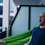 man in blue crew neck shirt standing beside green hammock