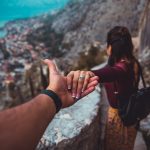 woman holding man's hand while looking on scenery of building beside body of water during daytime