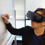 Person Wearing Black Vr Box Writing On White Board