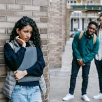 Latin American woman leaning on brick wall while hiding from multiracial classmates in college