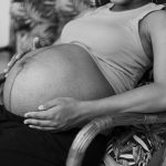 a black and white photo of a pregnant woman sitting in a chair