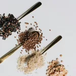 Top view of various dry grains on spoons against a white background, showcasing a variety of textures and colors.