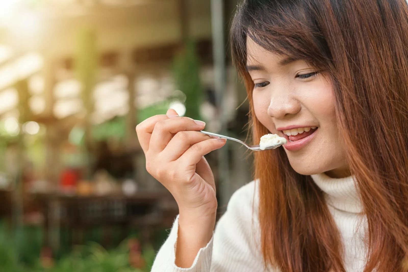15 Essential Steps to Improve Your Gut Microbiota 1 Happy woman enjoying a creamy dessert in a sunlit outdoor setting.