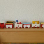 Red and white wooden toy train with numbers displayed on a wooden shelf.